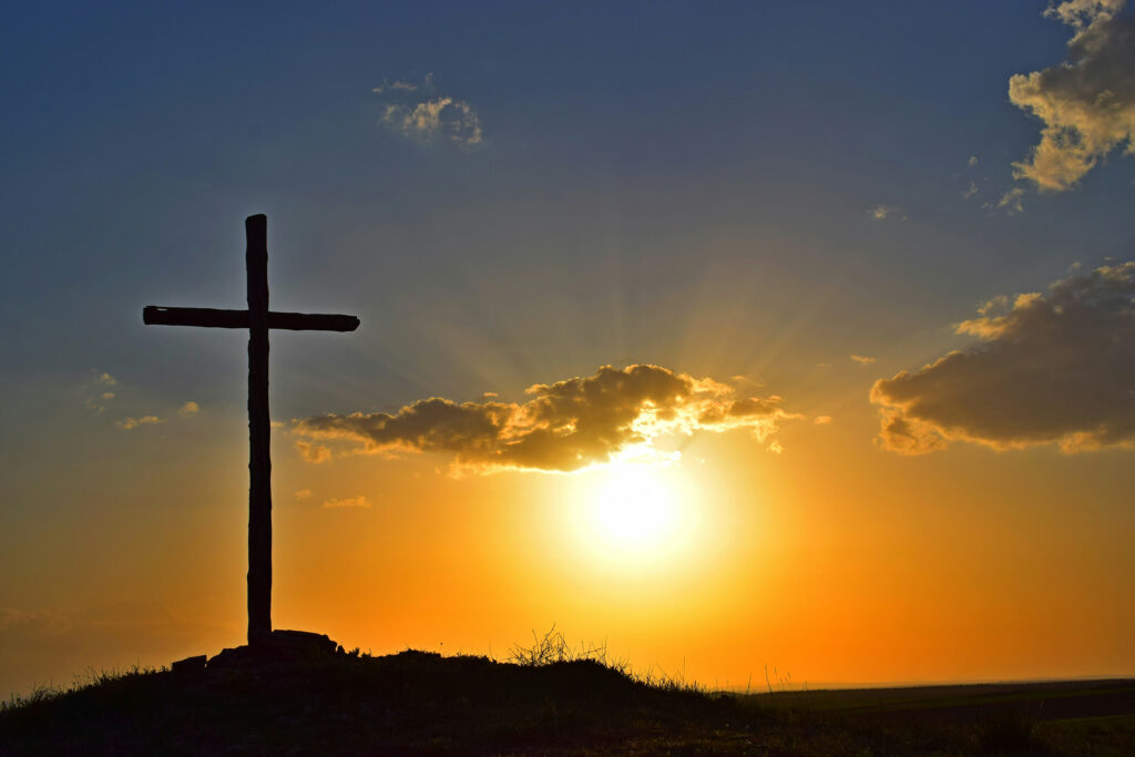 Ein Kreuz auf einem und im Hintergrund geht die Sonne unter.
© unsplash.com/Cdoncel